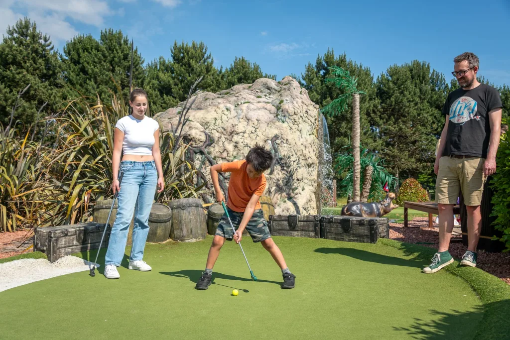 A family watching a young boy line up a shot on the Adventure Golf